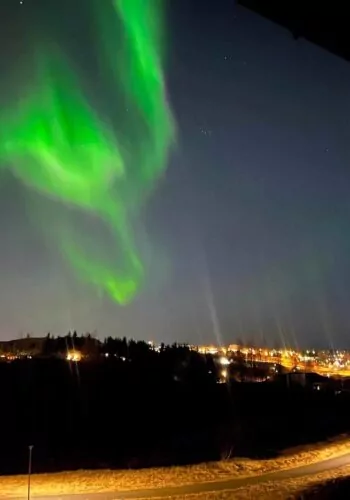 Green northern lights dancing over a town in Iceland at night.