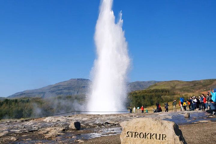Tall column of water from Strokkur geyser as tourists watch from a viewing area in Haukadalur, Iceland.